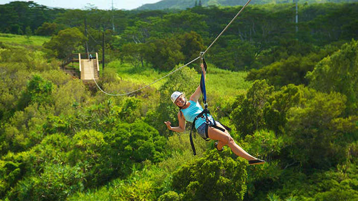 A woman hanging from a zipline in Kauai gives a shaka and a smile. 