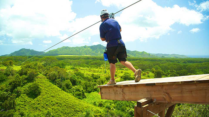 A person is running off the platform of a zipline tour over a green valley.